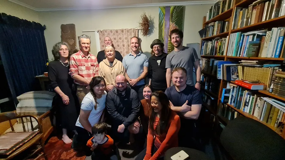 A group photograph indoors, some standing and some crouched in front, against a wall of bookshelves in a room with a low ceiling.