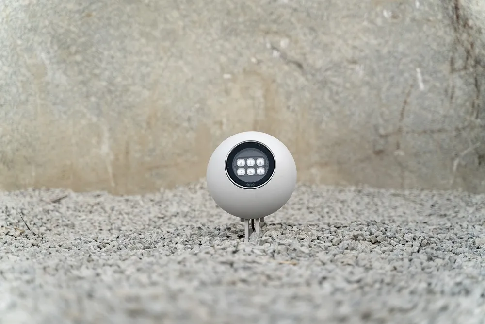 An ewo Chameleon in a pale finish, its round head on a short ground spike set in gravel against a rough stone wall.