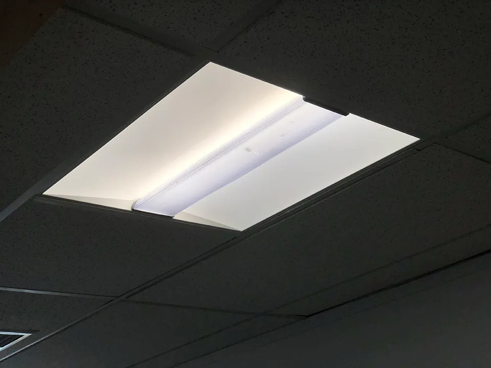 A troffer lit in a dark suspended ceiling, its curved white reflectors throwing the light out sideways rather than straight down.