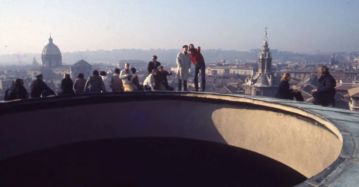 People standing at the rail of a Roman rooftop at dusk, the city and its domes behind them, with the raised lip of the Pantheon's oculus curving across the foreground.