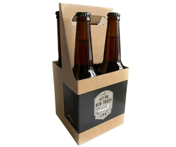 A four-pack of amber bottles in a kraft carrier, the label reading Old Dog New Tricks I.P.A.