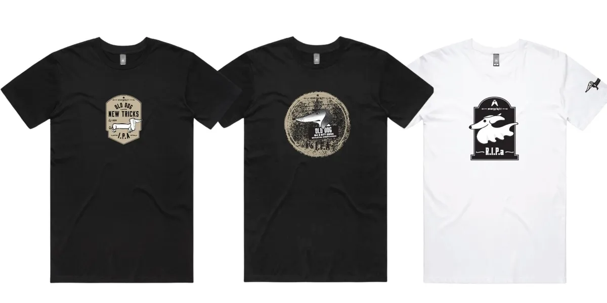 Three t-shirts laid out in a row, two black and one white, each printed with one of the beer labels from the collection.
